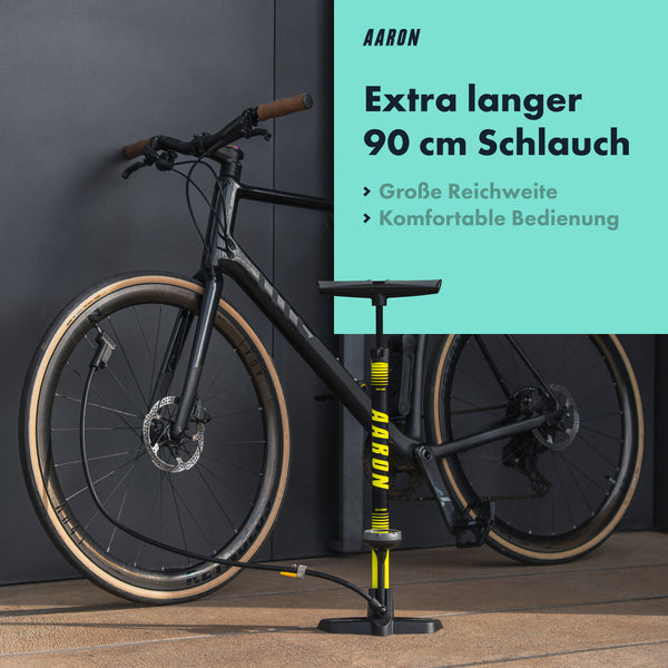 AARON Sport One 3.0 Fahrradpumpe - Gelb mit extra langem 90 cm Schlauch neben schwarzem Fahrrad vor dunklem Hintergrund