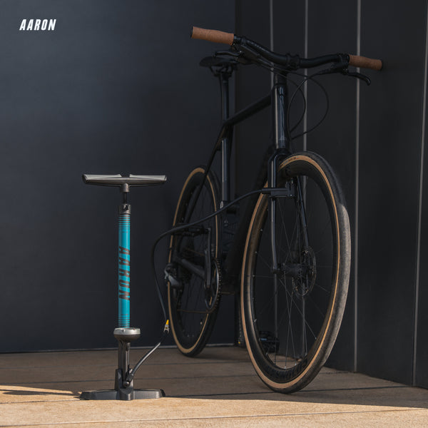 AARON Sport One 3.0 Fahrradpumpe - Blau neben schwarzem Fahrrad vor dunklem Hintergrund stehend