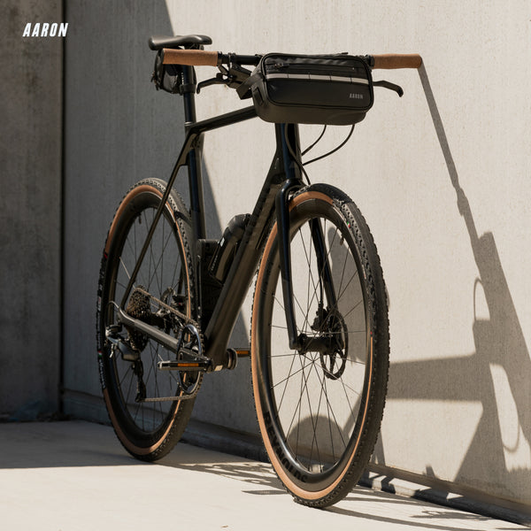 Schwarzes Fahrrad mit AARON Urban 3.0 Fahrradpedale - Schwarz, braune Reifen und Tasche am Lenker vor Betonwand