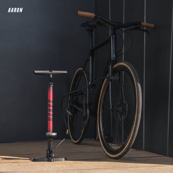 AARON Sport One 3.0 Fahrradpumpe - Rot stehend neben schwarzem Fahrrad mit braunen Griffen vor dunklem Hintergrund